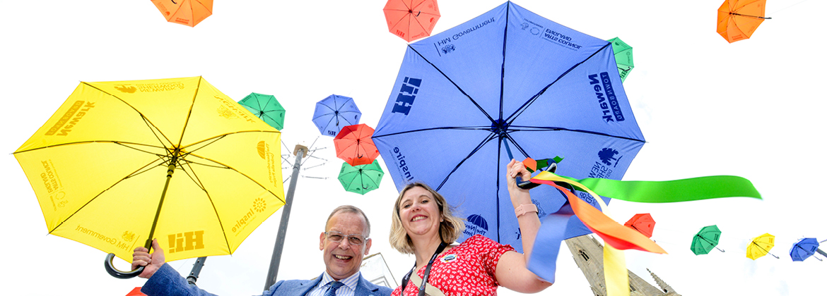 A man and a woman stand smiling beneath an array of colourful umbrellas